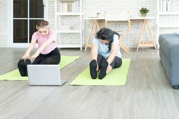 Young Asian and Senior woman exercising at home watching video follow trainer online on laptop computer. Senior health care and sport at home concept.