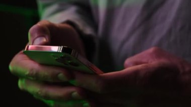 Man using mobile phone typing text or checking social media in neon lights. High quality 4k footage