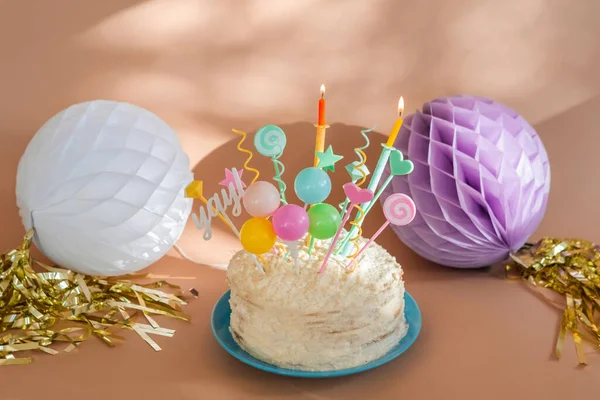 Homemade cream cake with candles. Party decor with paper balloons with fringe. Sus rays.