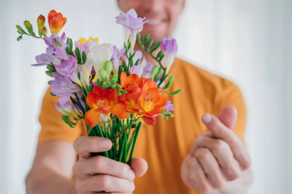 Front view of man hands giving a cute bouquet of spring flowers and showing heart symbol with finger hand. Selective focus.