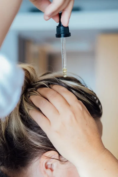 Woman applies oil to her hair with pipette. Beauty caring for scalp and hair