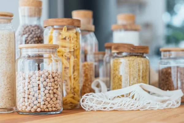 Zero waste concept. Textile eco-bags, glass jars with grocery on a wooden table in the kitchen. Eco-friendly reuse concept. Selective focus.