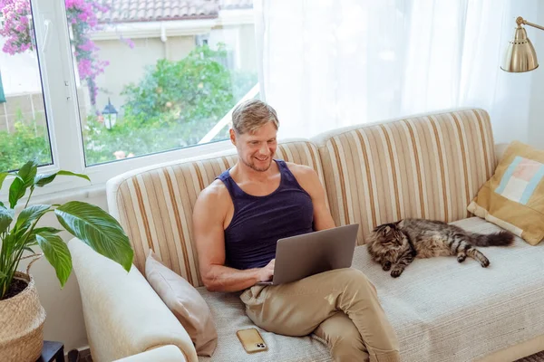 Mann Sitzt Mit Laptop Neben Katze Auf Dem Heimischen Sofa lizenzfreie Stockbilder