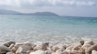 Güzel, huzurlu bir plaj sahnesi. Çakıl taşları üzerinde turkuaz su dalgalanması. Mavi denizin üzerindeki ufuktaki adalar. düşük açı