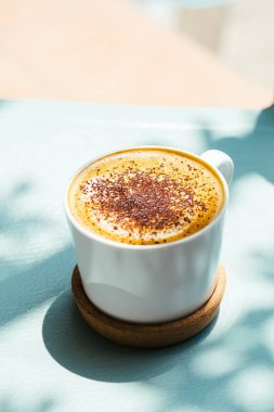 Mavi masanın üzerinde güzel gölgelerle süslenmiş fincan kapuçino kahvesi manzarası.