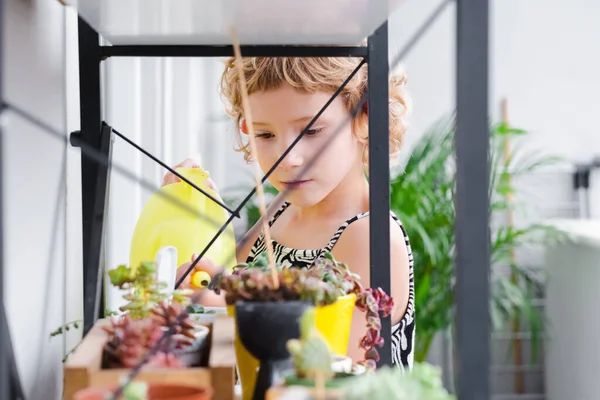 stock image Charming little girl watering plants from a watering can on the balcony close-up, taking care of home plants carefully. Caucasian happy child loves to plant and water flowers.