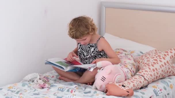 Nettes Kleines Mädchen Liest Eine Bildungszeitschrift Auf Dem Bett Schlafzimmer — Stockvideo