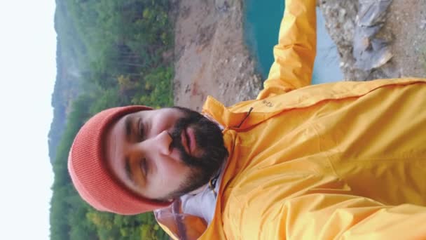 登山者在山顶上自拍自画像 戴着红帽子和黄色夹克的家伙为他的旅行日志制作视频报道或拍摄视频内容 — 图库视频影像