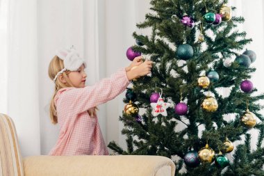 Küçük kız rahat pijamalarıyla Noel ağacını süslüyor.