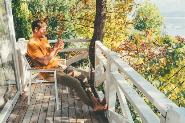 Handsome man talking over mobile phone while sitting in balcony at log cabin