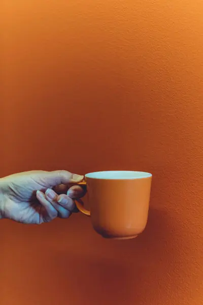 Orange coffee mug mockup for design demonstration. Cup mock up in female hands on orange wall background.