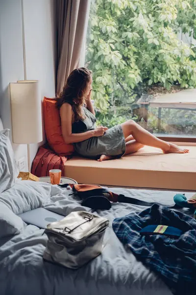 girl student sits by the window and talks on the phone in a room with a mess.
