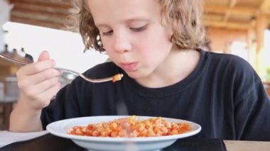 Kafede domates soslu makarna yiyen kıvırcık saçlı çocuk. Çocuk menüsü.