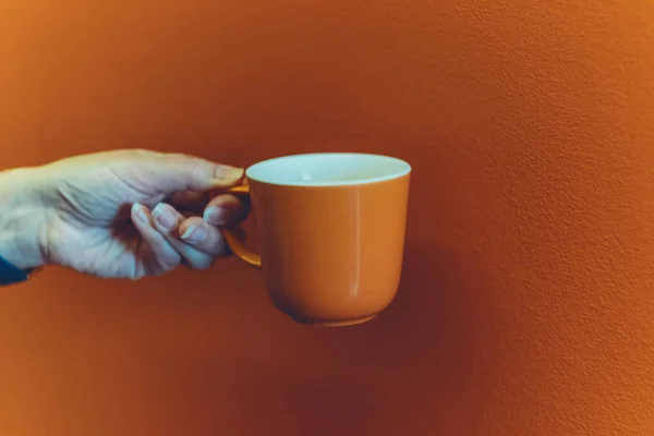 Orange coffee mug mockup for design demonstration. Cup mock up in female hands on orange wall background.