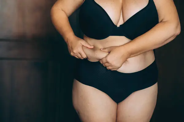 Woman pinching belly fat, a common concern for body image and health, in a moment of personal body awareness.