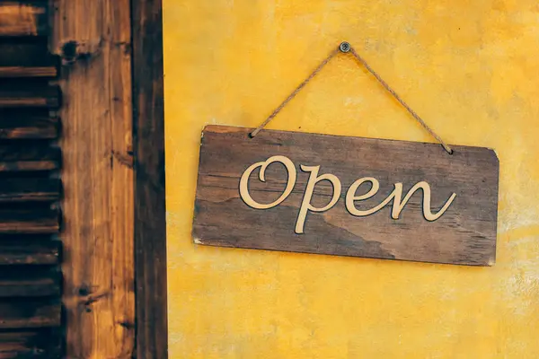 Rustic wooden Open sign hanging. A warm, inviting rustic wooden Open sign adorns a vibrant yellow stucco wall.