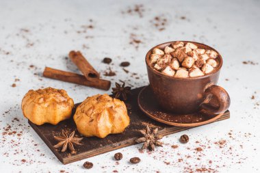 Bir fincanda krema ve üzerinde kakao tozu, tarçın çubuğu ve beyaz masada yıldız anason serpiştirilmiş tatlı olan sıcak çikolata içeceği..