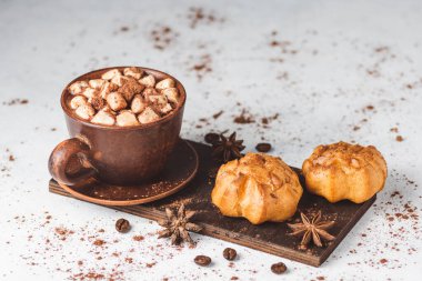 Bir fincanda krema ve üzerinde kakao tozu, tarçın çubuğu ve beyaz masada yıldız anason serpiştirilmiş tatlı olan sıcak çikolata içeceği..
