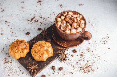 Bir fincanda krema ve üzerinde kakao tozu, tarçın çubuğu ve beyaz masada yıldız anason serpiştirilmiş tatlı olan sıcak çikolata içeceği..