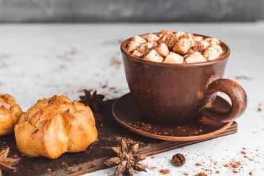 Bir fincanda krema ve üzerinde kakao tozu, tarçın çubuğu ve beyaz masada yıldız anason serpiştirilmiş tatlı olan sıcak çikolata içeceği..