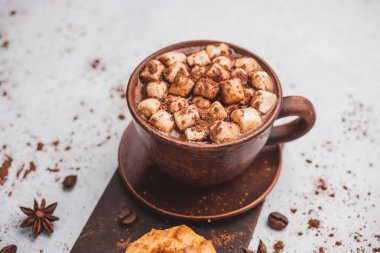Bir fincanda krema ve beyaz masa üzerine kakao tozu serpilmiş tatlı ekmekleri olan sıcak çikolata içeceği..