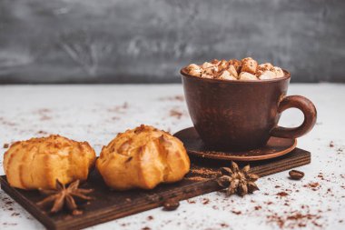 Bir fincanda krema ve beyaz masa üzerine kakao tozu serpilmiş tatlı ekmekleri olan sıcak çikolata içeceği..