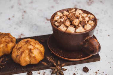 Bir fincanda krema ve beyaz masa üzerine kakao tozu serpilmiş tatlı ekmekleri olan sıcak çikolata içeceği..