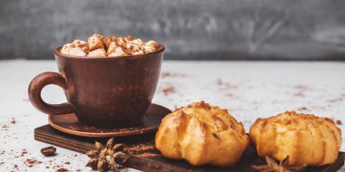 Bir fincanda krema ve beyaz masa üzerine kakao tozu serpilmiş tatlı ekmekleri olan sıcak çikolata içeceği..