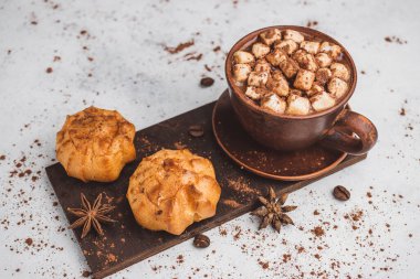 Bir fincanda krema ve beyaz masa üzerine kakao tozu serpilmiş tatlı ekmekleri olan sıcak çikolata içeceği..