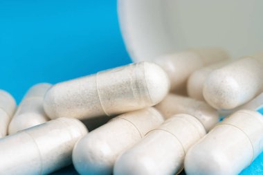 Beyaz haplar, ilaç kapsülleri, mavi arka planda vitaminler veya uyuşturucular, ilaç tedavisi, sağlık konsepti.