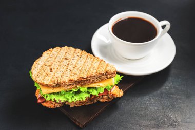 Peynirli ızgara sandviç, salata, salata, jambon ve koyu arkaplanda kahve fincanı. Kopyalama alanı ile öğle yemeği kavramı.