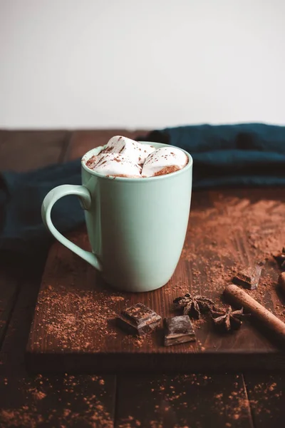 Hot chocolate drink with marshmallow in a cup on wooden board, dark background.