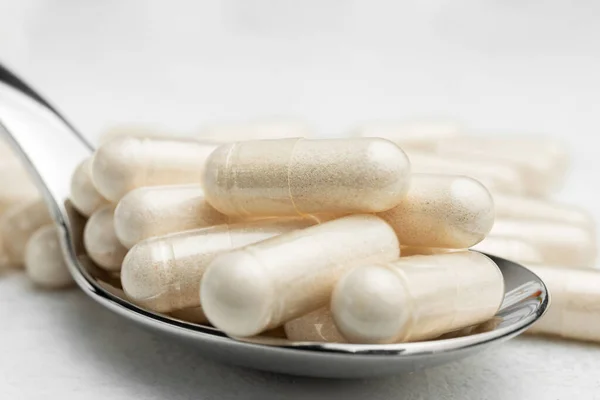 White medicine capsules, vitamin pills or drugs in a spoon, medication treatment, health care concept.