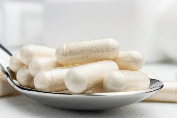 White medicine capsules, vitamin pills or drugs in a spoon, medication treatment, health care concept.