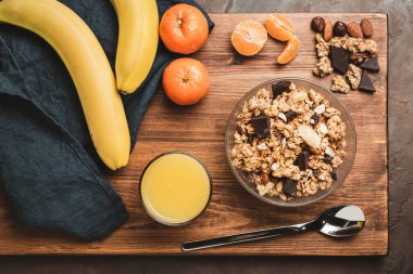 Granola cereal oatmeal with chocolate, banana and nuts in a bowl on dark wooden board, top view.