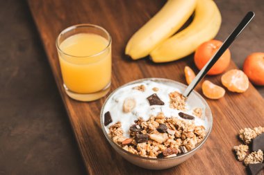 Granola cereal oatmeal with white yogurt, chocolate, banana fruit and nuts in a bowl on dark wooden board.