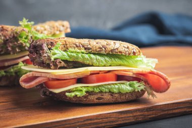 Sandwich with a ham, cheese, tomato, salad lettuce on a wooden board. Lunch concept with copy-space.
