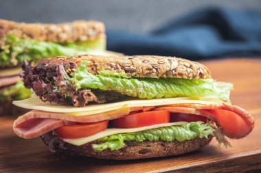 Sandwich with a ham, cheese, tomato, salad lettuce on a wooden board. Lunch concept with copy-space.