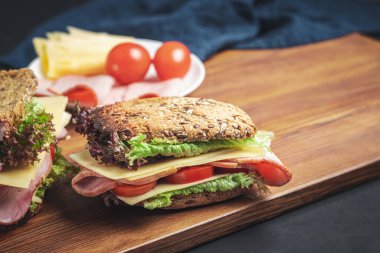 Sandwich with a ham, cheese, tomato, salad lettuce on a wooden board. Lunch concept with copy-space.