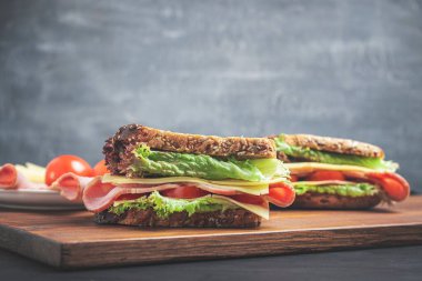 Sandwich with a ham, cheese, tomato, salad lettuce on a wooden board. Lunch concept with copy-space.