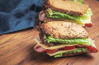 Sandwich with a ham, cheese, tomato, salad lettuce on a wooden board.