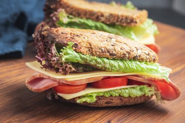 Sandwich with a ham, cheese, tomato, salad lettuce on a wooden board.