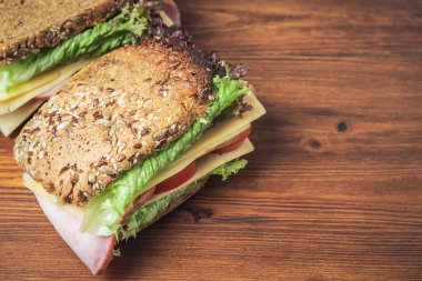 Sandwich with a ham, cheese, tomato, salad lettuce on a wooden board.
