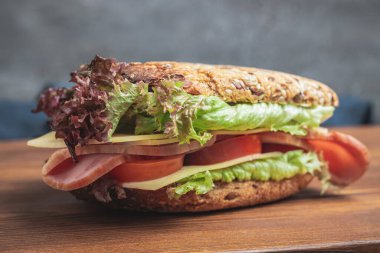 Sandwich with a ham, cheese, tomato, salad lettuce on a wooden board.