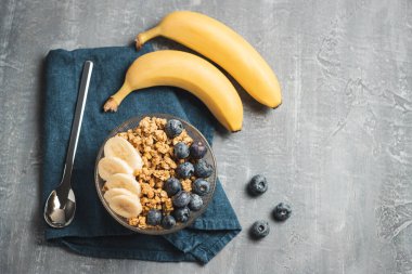 Granola cereal oatmeal with blueberries and banana fruits in a bowl on a grey background, top view.