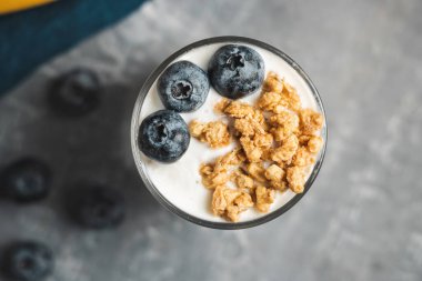 Granola cereal oatmeal with white yogurt, blueberries in a glass on a grey background, top view.