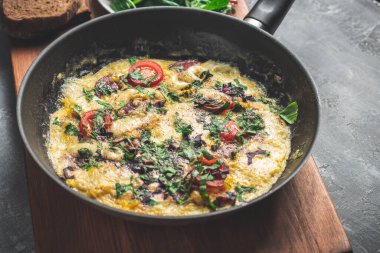 Cooked omelette with sausage, cheese, tomato and herbs in a pan, on wooden board.