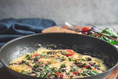 Cooked omelette with sausage, cheese, tomato and herbs in a pan, on wooden board.