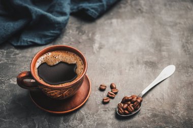 Kahverengi kilden bir fincanda sade kahve ve koyu arkaplanda kaşık kahve çekirdekleri..