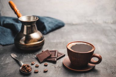 Kil fincanda sade kahve, Türk jezve kahve demliği, çikolata parçaları ve koyu arkaplanda kaşık kahve çekirdekleri..